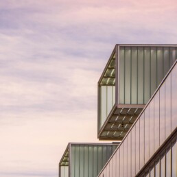 Glass office building with cantilevered box windows under a pink evening sky