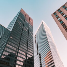 Looking up at three glass and steel skyscrapers against a clear blue sky