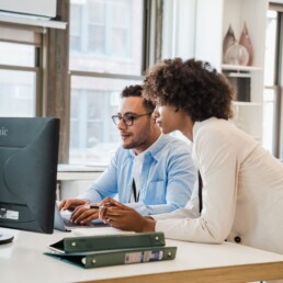 Two coworkers reviewing work together at a computer in a modern office
