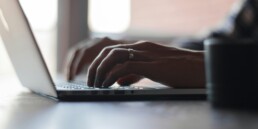 Close-up of a person's hands typing on a laptop keyboard at a desk