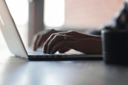 Close-up of a person's hands typing on a laptop keyboard at a desk